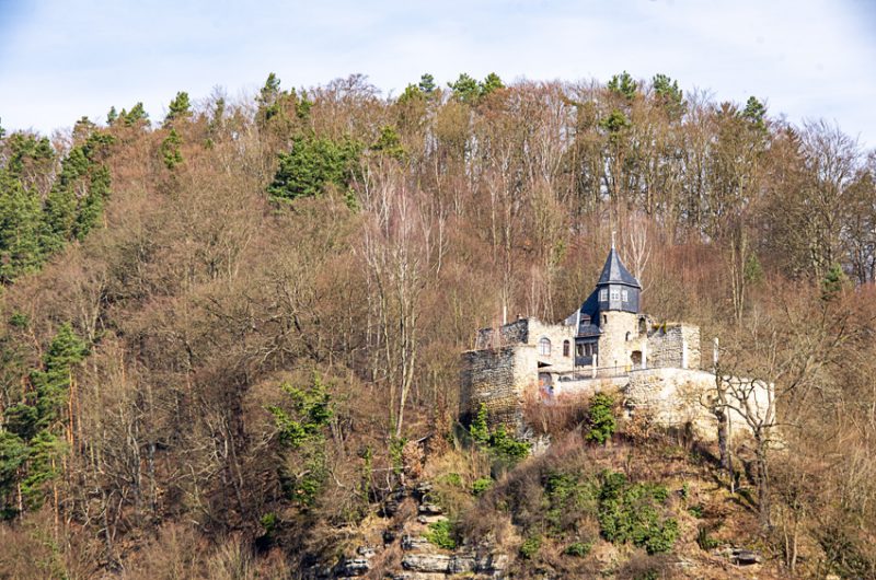 A manor house or small castle with a dark grey spire roof over a central tower, overlooking the Elbe River.